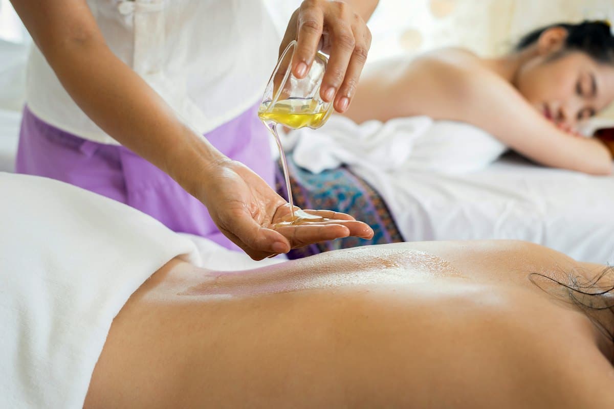 Hai khách nằm cạnh nhau trong phòng massage, kỹ thuật viên rót tinh dầu