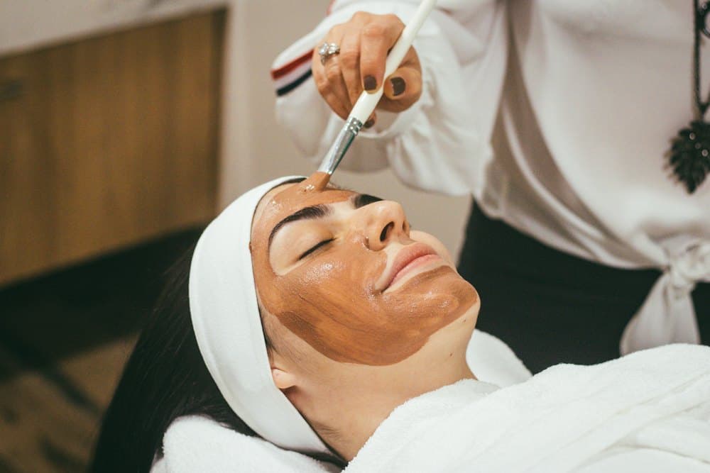 Kỹ thuật viên dùng cọ đắp mặt nạ cho khách nằm nhắm mắt
