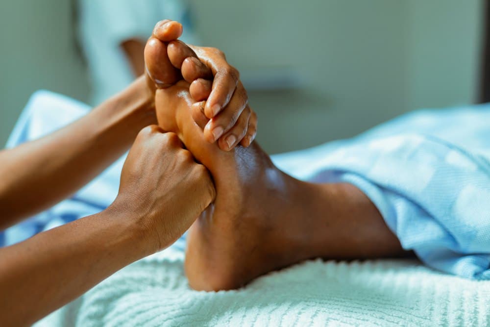 Đôi tay xoa dầu massage bàn chân khách trên khăn trắng