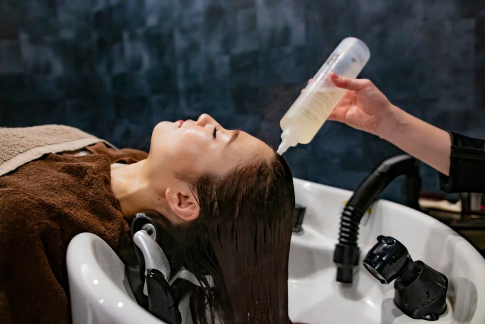 Khách nằm tại bồn gội, kỹ thuật viên rưới dầu gội lên tóc
